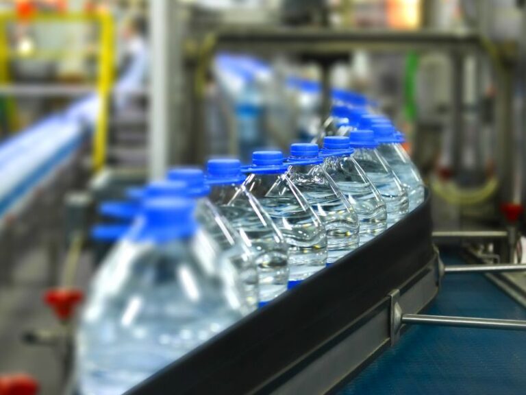 Clear-plastic water bottles with blue caps lined up on a conveyor belt in a production facility
