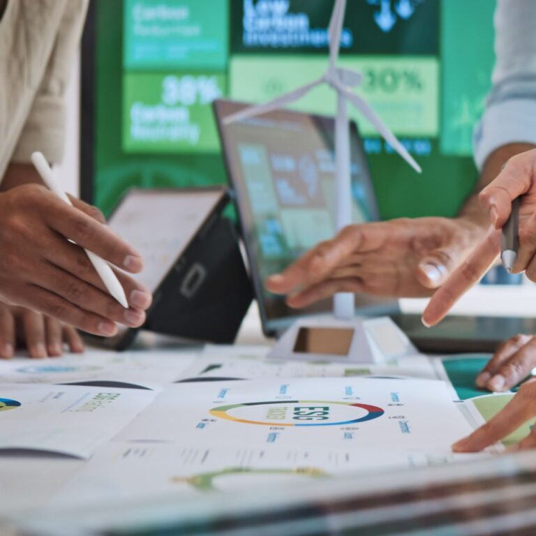 Hands reviewing sustainability charts with laptop and wind turbine model on table